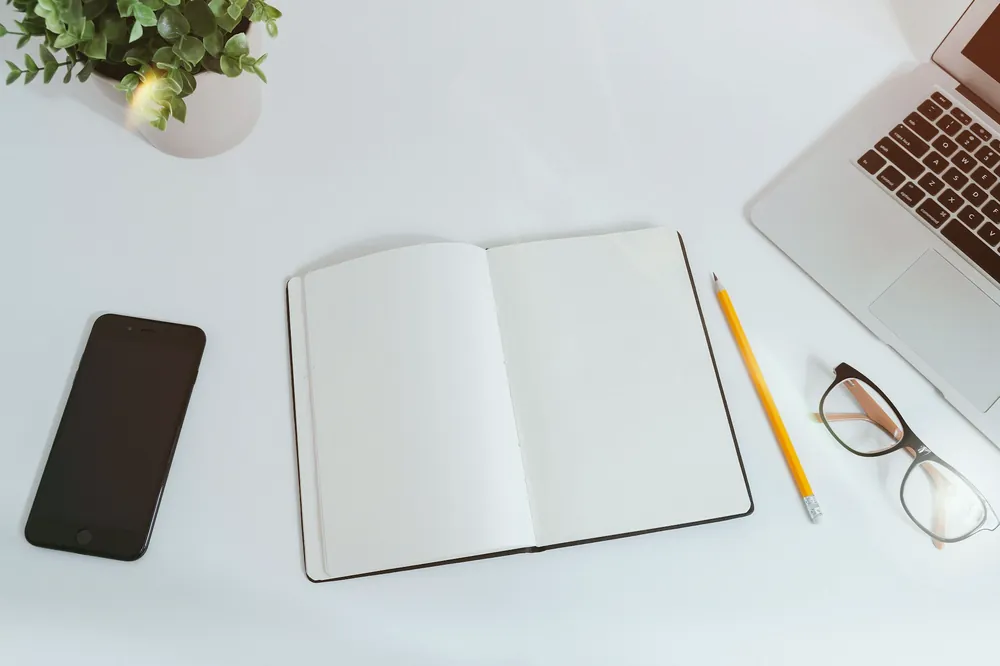 Carnet ouvert, stylo et lunettes sur un bureau blanc