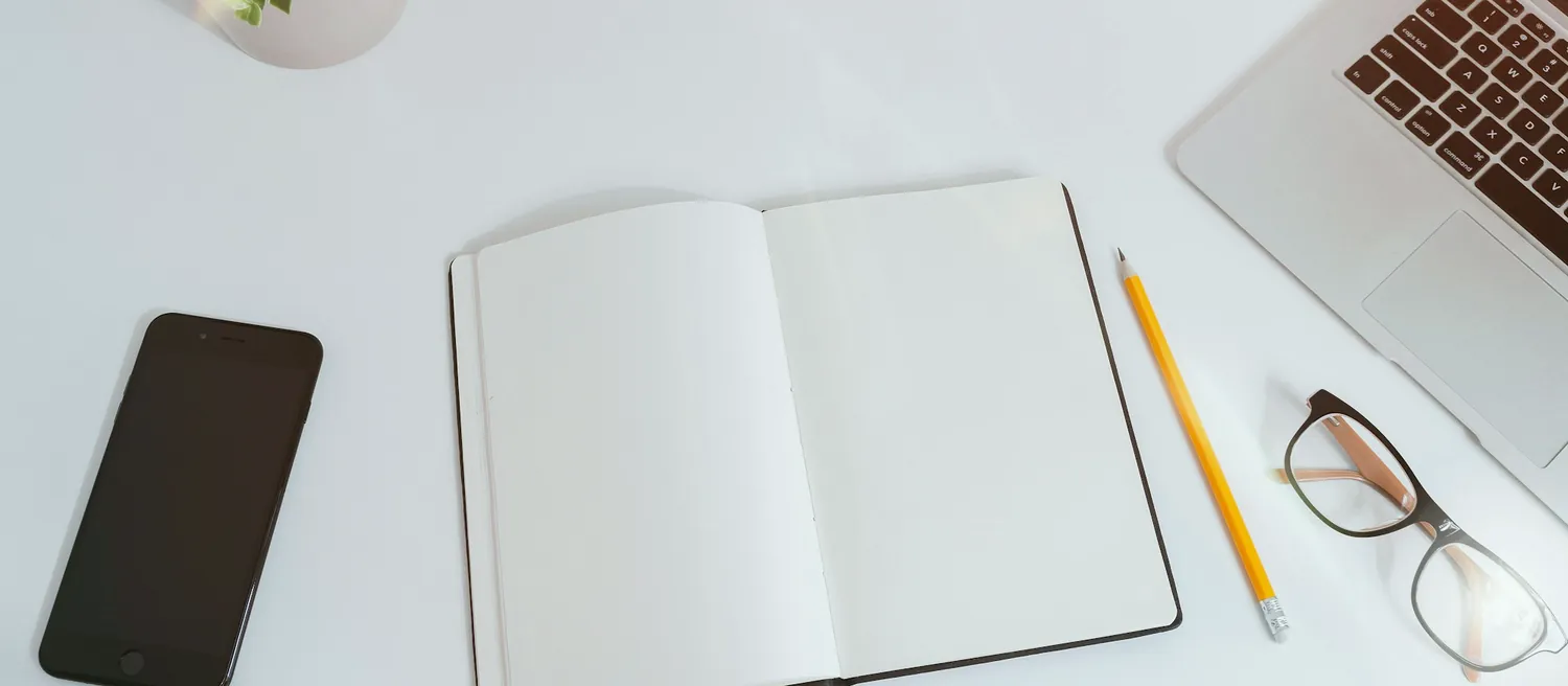 Carnet ouvert, stylo et lunettes sur un bureau blanc